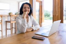 Glückliche reife Freiberuflerin surft im Internet auf einem Netbook und arbeitet an einem neuen Projekt, während sie zu Hause am Tisch sitzt — Stockfoto