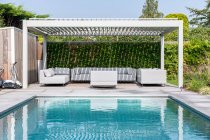 Двор дорогого современного особняка с бассейном и зоной отдыха с удобными диванами и креслами под голубым небом — стоковое фото