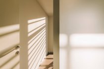 Интерьер дверной ручки в пустом просторном коридоре лофта с геометрическими тенями и солнечным светом на белых стенах — стоковое фото