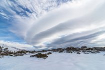 Живописный пейзаж снежной долины со скалами, расположенными в горной местности в зимнее время под облачно-голубым небом при дневном свете — стоковое фото
