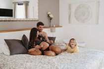 Bambino allegro in pigiama divertirsi sul letto contro la madre incinta che interagisce con il marito in casa — Foto stock