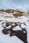 Paisaje de ladera nevada de colina en las tierras altas bajo cielo nublado a la luz del día y un río de agua helada - foto de stock