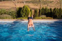 Full body back view of unrecognizable barefoot and shirtless senior male jumping in swimming pool with clear blue water — Stock Photo