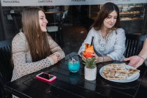 Crop content migliori amiche con gustose bevande mentre il cameriere porta spuntini in mensa di strada — Foto stock