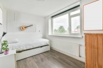 Interieur eines modernen hellen Schlafzimmers mit bequemem Bett in Wandnähe mit Gitarre und Fenster im Tageslicht — Stockfoto