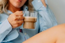 Colheita fêmea adulta com cabelo ondulado bebendo café saboroso enquanto olha para a frente em casa — Fotografia de Stock