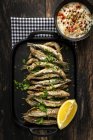 Top view of tasty fried anchovies with juicy lemon piece and chopped parsley on tray against savory sauce — Stock Photo
