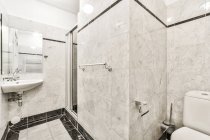Interior da casa de banho de luz contemporânea com WC perto de cabine de duche e pia sob espelho no apartamento moderno — Fotografia de Stock