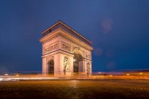 Antiguo arco de piedra con adornos y estatuas contra la plaza bajo el cielo azul al atardecer en invierno París Francia - foto de stock