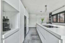 Светлый интерьер кухни с металлической раковиной и встроенной бытовой техникой в современном доме — стоковое фото