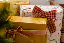 Коллекция рождественских подарков, завернутых в бумагу и ленты, помещенных возле ветвей елки — стоковое фото
