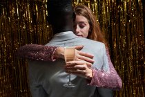 Стильна багатонаціональна пара зі склом шампанського обіймає її з невідомим чорношкірим хлопцем під час святкування Нового року. — стокове фото