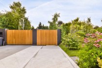 Puertas de madera de la casa de campo residencial contemporánea con arquitectura minimalista rodeada de exuberantes árboles verdes en el día soleado - foto de stock