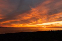 Vue spectaculaire des silhouettes du voyageur contemplant l'océan depuis la plage sous un ciel nuageux coloré au coucher du soleil — Photo de stock