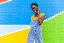 Feliz joven mujer afroamericana sonriendo mientras está de pie en la pared brillante colorido - foto de stock