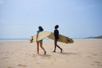 Visão traseira de jovens surfistas multiétnicos do sexo feminino com pranchas de surf falando enquanto passeiam na costa arenosa e olhando uns para os outros — Fotografia de Stock