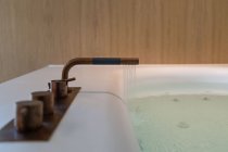 Interior de baño contemporáneo con bañera de hidromasaje con agua limpia contra la pared de luz en el apartamento - foto de stock