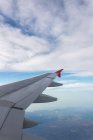A través de la ventana del avión vista de nubes esponjosas sobre el mar y el terreno durante el viaje durante el día - foto de stock