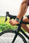 Side view of crop unrecognizable sportsman in wearable tracker riding modern bike during training on roadway in countryside — Stock Photo