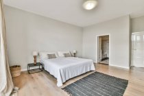Moderno spazioso interno camera da letto en suit arredato con comodo letto con comodino vicino tappeto e bagno — Foto stock
