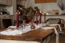 Toalha de mesa branca e placas colocadas na mesa festiva decorada com velas em chamas e galhos secos de árvore — Fotografia de Stock
