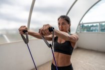 Determinata giovane atleta etnica femminile in abbigliamento sportivo che lavora con elastico mentre guarda avanti — Foto stock