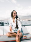 Besinnlich fröhliche Teenagerin sitzt mit gekreuzten Beinen auf Bank des Motorbootes auf dem Meer und schaut weg in Teneriffa Spanien — Stockfoto