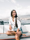 Contemplativa adolescente feliz sentada com pernas cruzadas no banco de lancha no oceano, enquanto olha para longe em Tenerife Espanha — Fotografia de Stock