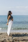 Side view of ethnic female leaning back while standing in Ashta Chandrasana pose during yoga practice on sandy coast against ocean — Stock Photo