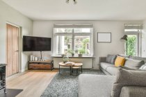 Серый диван с подушками и телевизором в стильной гостиной в роскошной квартире днем — стоковое фото