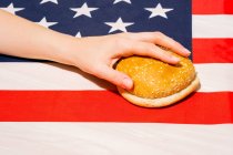 Cultive a pessoa irreconhecível com metades de pão de gergelim na bandeira dos EUA com ornamento de estrela e listra no Dia da Independência — Fotografia de Stock