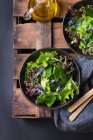 Сверху вкусный вегетарианский салат с зелеными и красными листьями салата и съедобными цветами против кувшина с маслом — стоковое фото