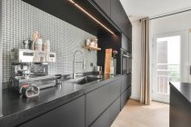 Moderne Kaffeemaschine auf dunkler Küchentheke neben Spüle in moderner Küche mit schwarzen Schränken in der Wohnung tagsüber platziert — Stockfoto