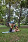 Pleine longueur de couple concentré en vêtements de sport faire asana tout en pratiquant l'acroyoga ensemble dans un parc vert en plein jour — Photo de stock