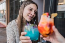 Веселые девушки-подростки, взаимодействующие во время звона стаканов вкусных освежающих напитков за столом в городской столовой — стоковое фото