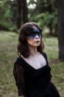Mystische Hexe im langen schwarzen Kleid und mit gemaltem Gesicht, die in dunklen, düsteren Wäldern wegschaut — Stockfoto