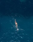 Drohnenbild eines anonymen männlichen Touristen mit nacktem Oberkörper, der bei Tageslicht im welligen Ozean schwimmt — Stockfoto