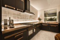 Интерьер элегантной просторной кухни с современной техникой и минималистской мебелью с бронзовыми деталями в современном особняке — стоковое фото