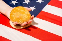 Crop unrecognizable person with sesame bun halves on USA flag with star and stripe ornament on Independence Day — Stock Photo