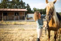 Side view of content mature female stroking stallion muzzle with smooth brown coat against hay in riding school on sunny day — Stock Photo