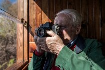 Homem tirando fotos com sua velha câmera pela janela de um velho vagão de trem de madeira — Fotografia de Stock