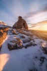 Paisagem pitoresca pequena casa de pedra envelhecida colocada no topo nevado das montanhas sob o colorido céu nublado ao pôr do sol — Fotografia de Stock