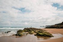 Scenery view of rocky formations on wet sandy beach against wavy ocean under cloudy sky in Cantabria Spain — Stock Photo