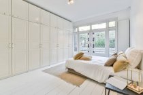 Interior minimalista de amplio dormitorio con cama acogedora y armario grande en moderno piso nuevo - foto de stock