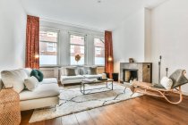 Интерьер просторной гостиной с камином и удобным диваном и креслами в современном доме — стоковое фото
