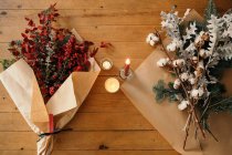 From above of festive Christmas bouquet with branches of cotton, fir and twigs of eucalyptus and bright red branches with berries placed on wooden table with candles in room — Stock Photo