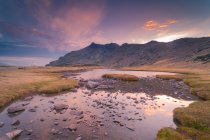 Cenário espetacular de lago calmo com rochas contra altas montanhas em Sierra de Guadarrama sob colorido céu nublado ao nascer do sol — Fotografia de Stock