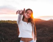 Зміст самиці з простягнутою рукою дивлячись на фотоапарат на горі проти океану на заході сонця в Тенерифе Іспанії — стокове фото