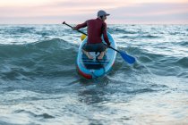 Вид ззаду на невизначений чоловічий серфер у гідрокостюмі та капелюсі на дошці для весла, що серфінгу на морському узбережжі — стокове фото