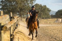 Feminino com treinador masculino montando garanhões no campo no dia ensolarado — Fotografia de Stock